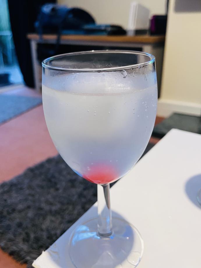 Glass of cloudy white liquid with a large ice cube and a cherry