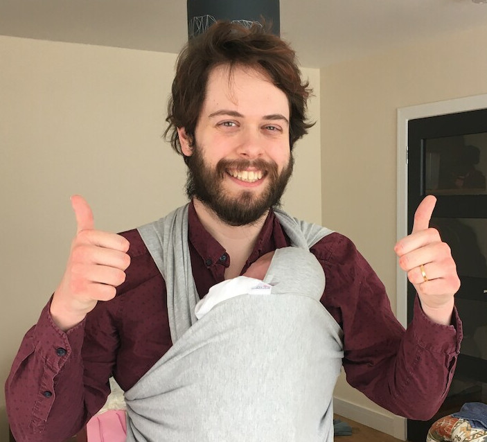 Photo of me giving a thumbs up, carrying a baby in a sling